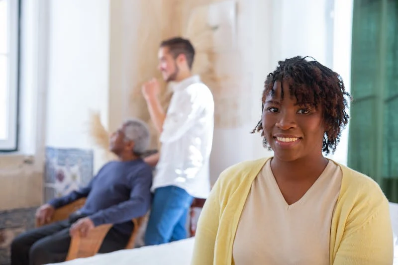 A smiling caregiver sitting with an older adult in a bright living room